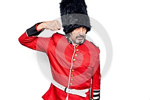 Middle age handsome wales guard man wearing traditional uniform over white background Strong person showing arm muscle, confident