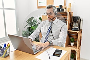 Middle age hispanic business man working at the office wearing operator headset afraid and shocked with surprise expression, fear