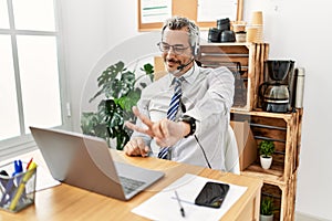 Middle age hispanic business man working at the office wearing operator headset smiling looking to the camera showing fingers