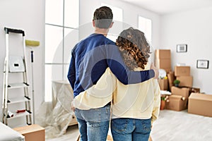 Middle age hispanic couple on back view hugging and standing at new home