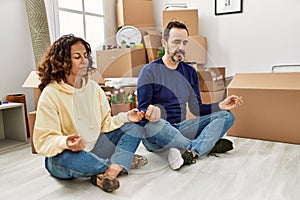 Middle age hispanic couple concentrated sitting on the floor doing yoga pose new home