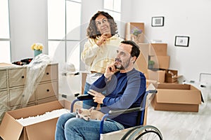 Middle age hispanic couple and dog sitting on wheelchair at new home serious face thinking about question with hand on chin,