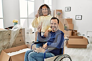 Middle age hispanic couple and dog sitting on wheelchair at new home surprised with an idea or question pointing finger with happy