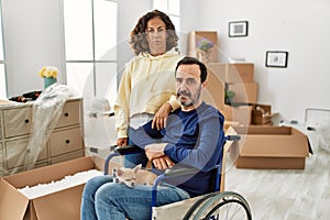 Middle age hispanic couple and dog sitting on wheelchair at new home thinking attitude and sober expression looking self confident