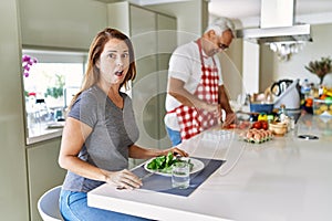 Middle age hispanic couple eating healthy salad at home scared and amazed with open mouth for surprise, disbelief face