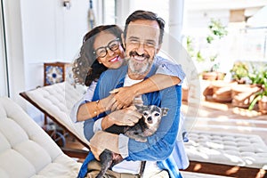 Middle age hispanic couple hugging each other sitting on hammock with dog at terrace