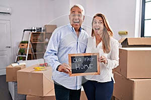 Middle age hispanic couple moving to a new home holding banner celebrating crazy and amazed for success with open eyes screaming