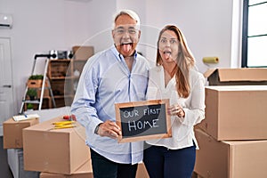 Middle age hispanic couple moving to a new home holding banner sticking tongue out happy with funny expression