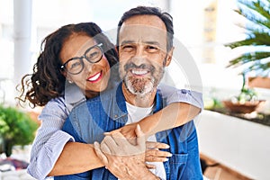 Middle age hispanic couple smiling confident hugging each other sitting on hammock at terrace