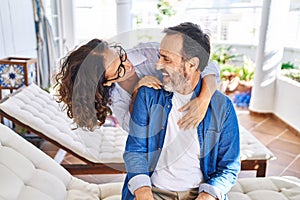 Middle age hispanic couple smiling confident hugging each other sitting on hammock at terrace