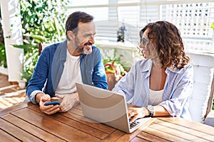 Middle age hispanic couple smiling confident using laptop and smartphone at terrace