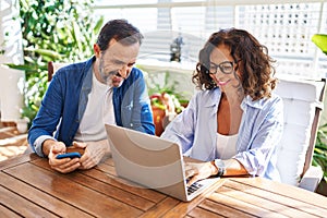 Middle age hispanic couple smiling confident using laptop and smartphone at terrace