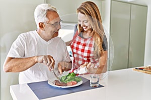 Middle age hispanic couple smiling happy eating beef with salad at the kitchen