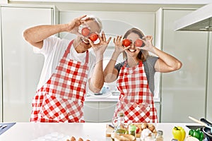 Middle age hispanic couple smiling happy holding tomatoes over eyes at the kitchen