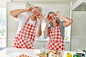 Middle age hispanic couple smiling happy holding tomatoes over eyes at the kitchen