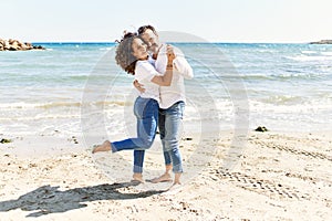 Middle age hispanic couple smiling happy and hugging standing at the beach