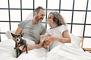 Middle age hispanic couple smiling happy lying on the bed with dogs at home