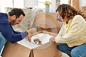 Middle age hispanic couple smiling happy playing with dog and foam package at new home
