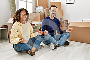 Middle age hispanic couple smiling happy sitting on the floor doing yoga pose new home