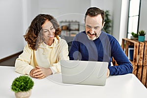 Middle age hispanic couple smiling happy using laptop at home