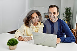 Middle age hispanic couple smiling happy using laptop at home