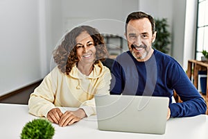 Middle age hispanic couple smiling happy using laptop at home