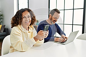 Middle age hispanic couple smiling happy using laptop and smartphone at home