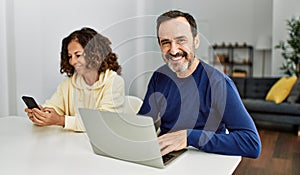 Middle age hispanic couple smiling happy using laptop and smartphone at home