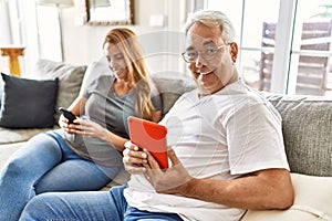 Middle age hispanic couple smiling happy using tablet and smartphone at home