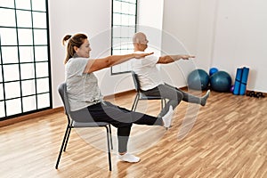 Middle age hispanic couple stretching using chair at sport center