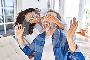 Middle age hispanic couple surprise with hands on eyes sitting on hammock at terrace