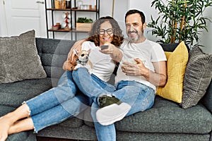 Middle age hispanic couple watching movie and eating popcorn sitting on the sofa at home