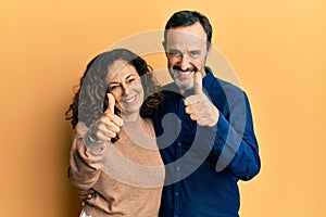 Middle age hispanic couple wearing casual clothes approving doing positive gesture with hand, thumbs up smiling and happy for