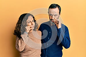 Middle age hispanic couple wearing casual clothes mouth and lips shut as zip with fingers