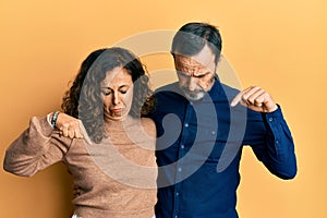 Middle age hispanic couple wearing casual clothes pointing down looking sad and upset, indicating direction with fingers, unhappy