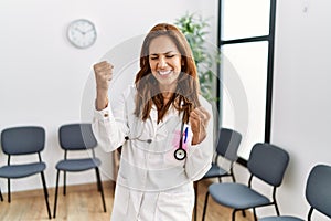 Middle age hispanic doctor woman at waiting room very happy and excited doing winner gesture with arms raised, smiling and