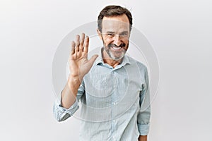 Middle age hispanic man with beard standing over isolated background waiving saying hello happy and smiling, friendly welcome