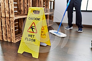 Middle age hispanic man cleaning floor with caution wet floor banner at home