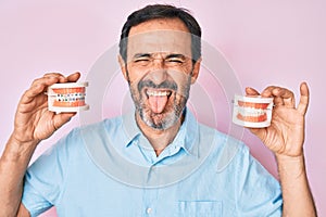 Middle age hispanic man holding orthodontic sticking tongue out happy with funny expression