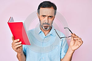 Middle age hispanic man reading book holding glasses depressed and worry for distress, crying angry and afraid