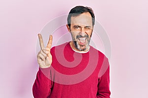 Middle age hispanic man wearing casual clothes smiling with happy face winking at the camera doing victory sign