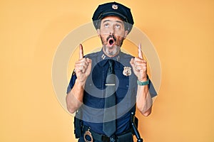 Middle age hispanic man wearing police uniform amazed and surprised looking up and pointing with fingers and raised arms