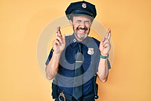 Middle age hispanic man wearing police uniform gesturing finger crossed smiling with hope and eyes closed