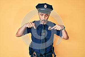 Middle age hispanic man wearing police uniform pointing down with fingers showing advertisement, surprised face and open mouth