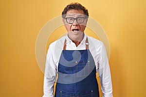 Middle age hispanic man wearing professional cook apron afraid and shocked with surprise expression, fear and excited face