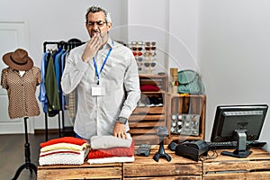 Middle age hispanic man working as manager at retail boutique bored yawning tired covering mouth with hand