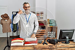 Middle age hispanic man working as manager at retail boutique smiling doing phone gesture with hand and fingers like talking on