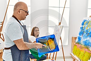 Middle age hispanic painter couple painting using paint roller at art studio