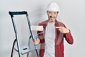 Middle age hispanic painter man holding roller using ladder pointing finger to one self smiling happy and proud