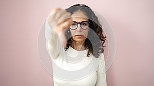 Middle age hispanic woman doing negative gesture with thumb down over isolated pink background